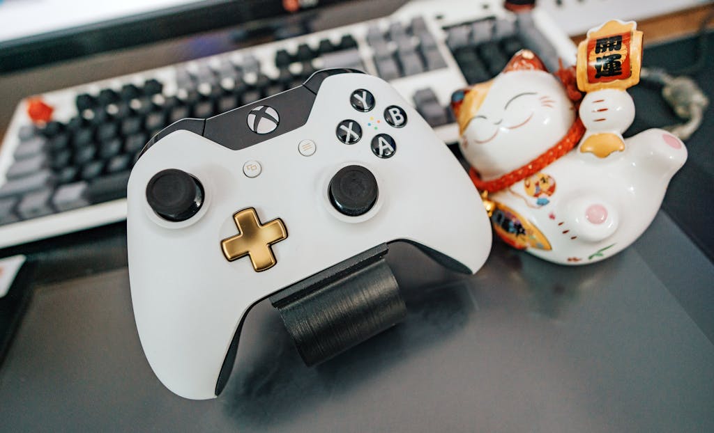 Close-up image of a sleek wireless game controller next to a traditional lucky cat figurine on a modern desk.